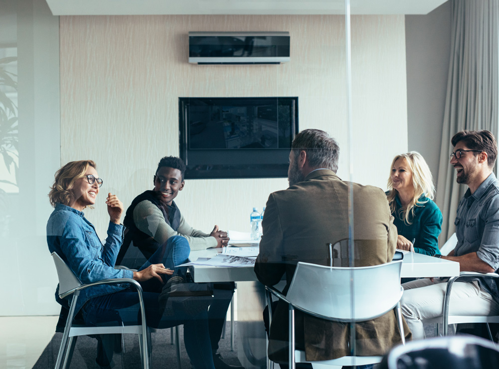 people sitting round a table in a meeting room with a TV screen on the wall