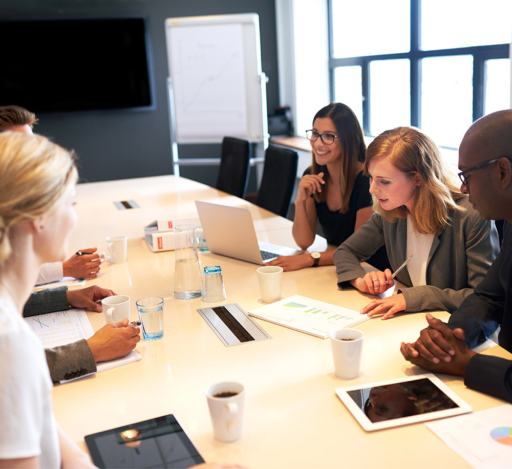group of office workers sitting round a table having a meeting with laptops and tablets